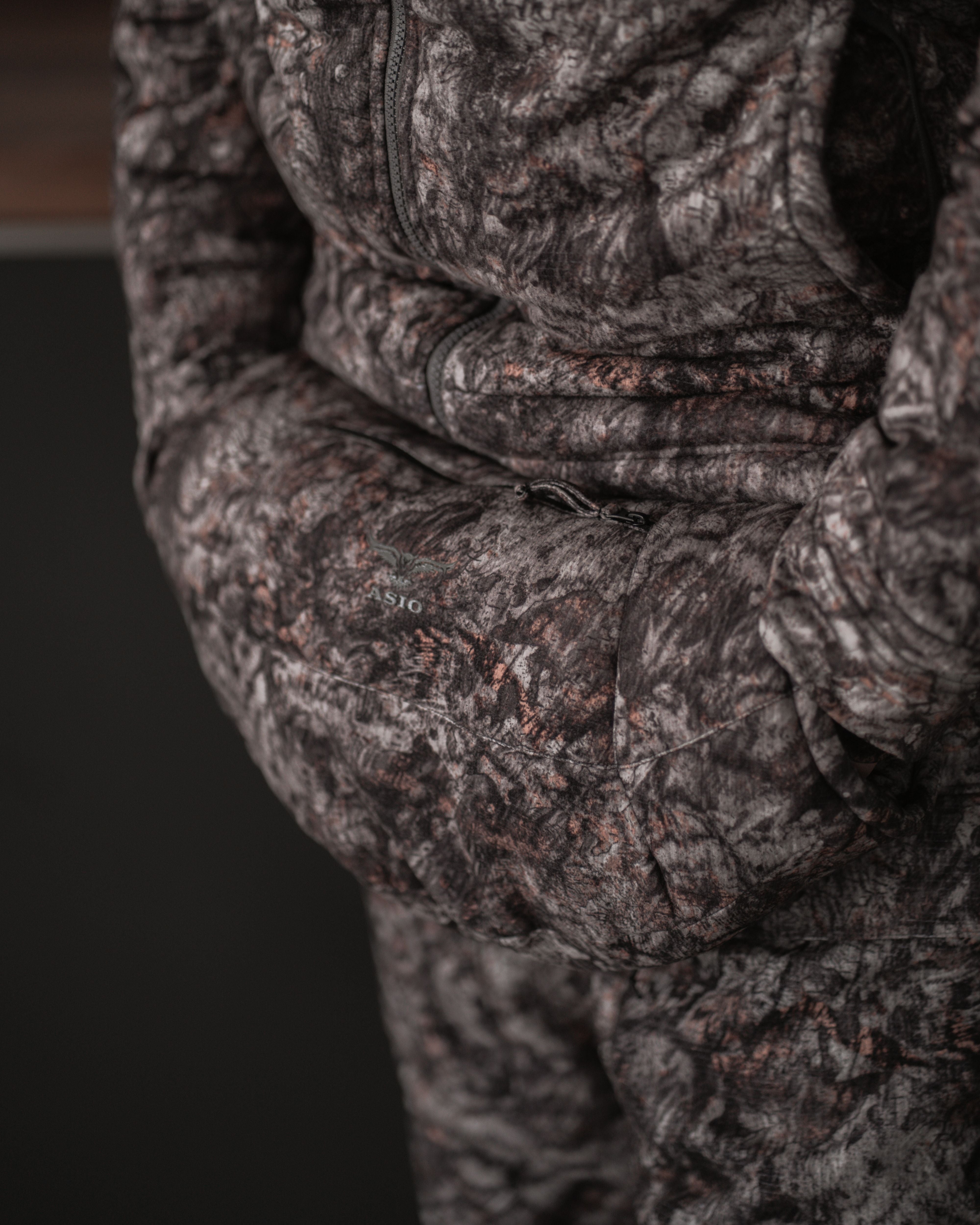 ASIO Gear handmuff worn at the waist in Raptor camo, showing sleek front pocket design in natural lighting.