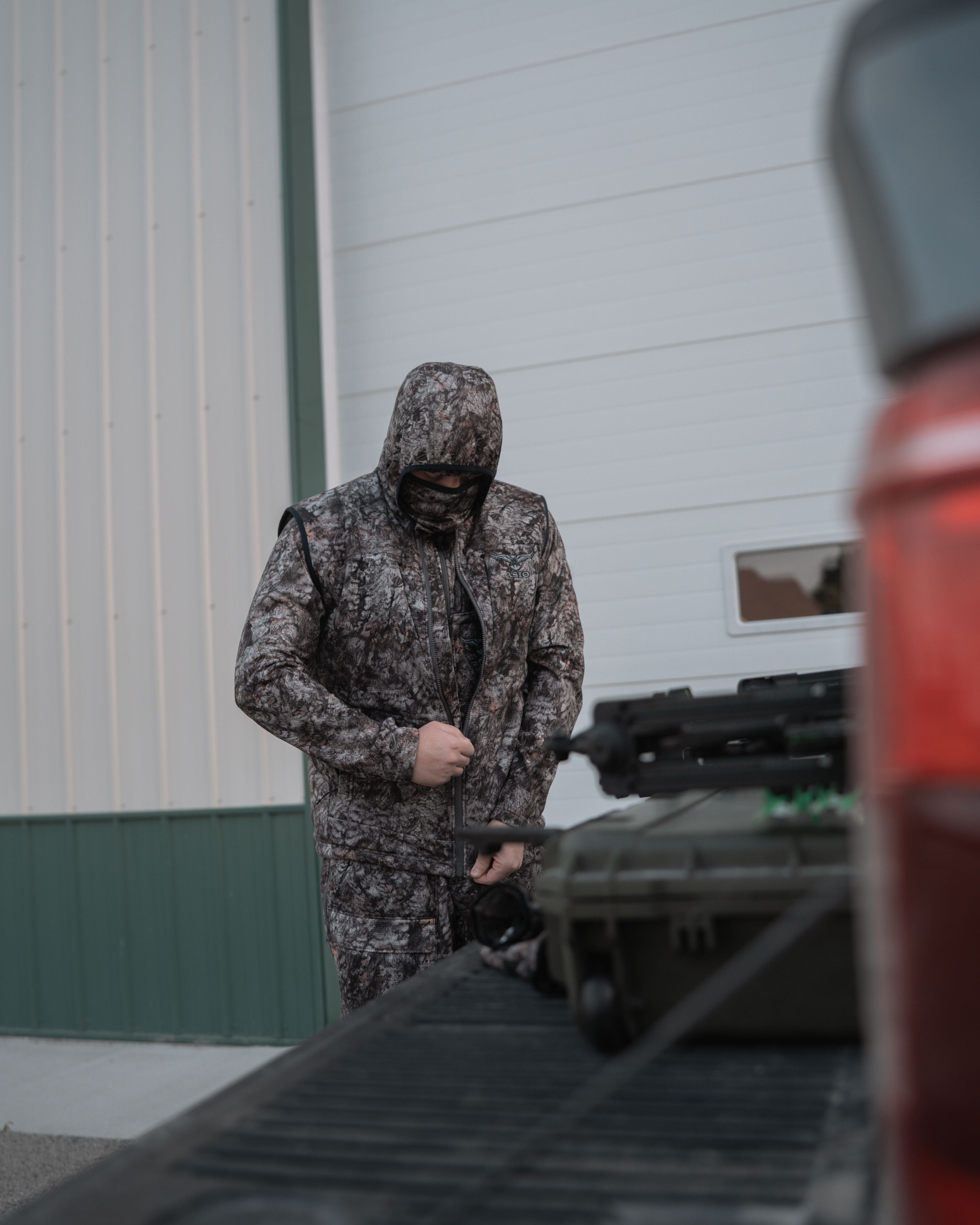 Bowhunter wearing the ASIO Gear heavyweight vest in Raptor camo while layering up near his vehicle.