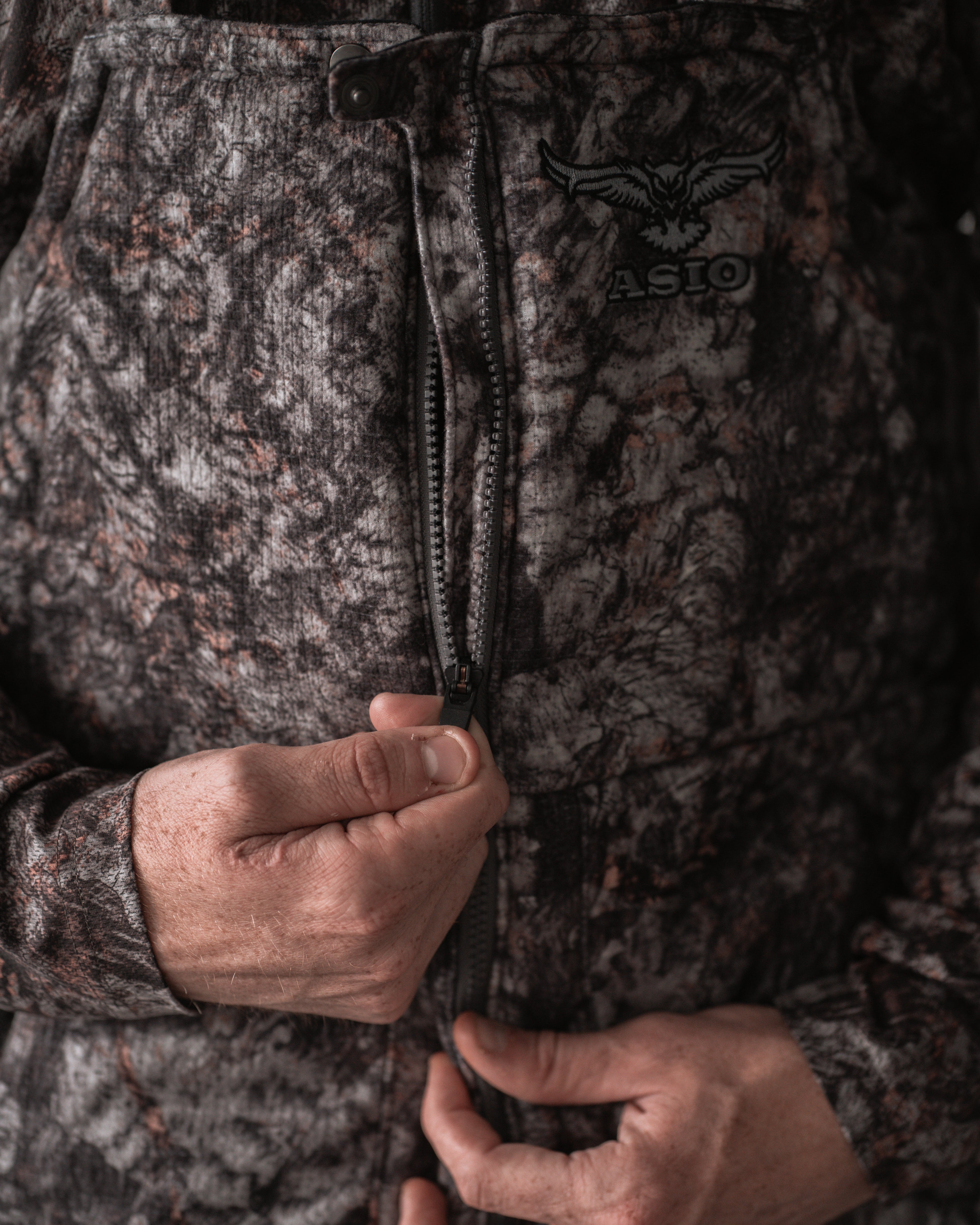 Close-up of ASIO Heavyweight Bib in RAPTOR camo highlighting zipper and pocket seam detail