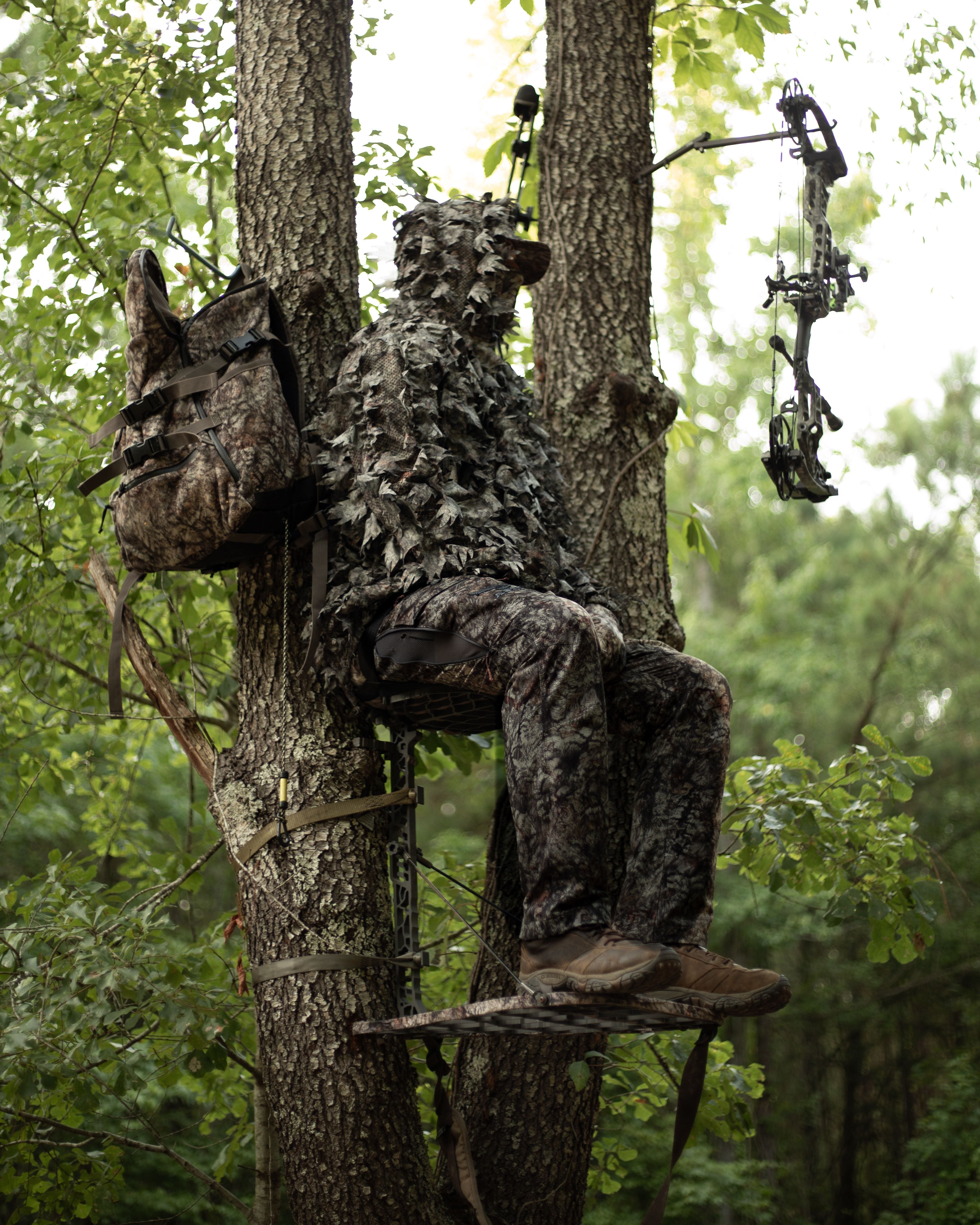 Hunter wearing ASIO Gear Leafy Jacket in Raptor camo sitting in a treestand, demonstrating peak concealment for bowhunting.