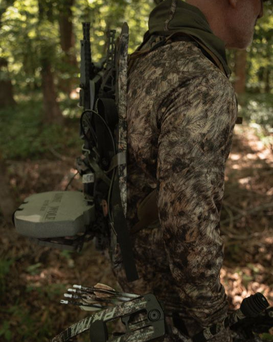 Hunter kneeling in ASIO Gear RAPTOR camo lightweight hoodie preparing gear for early season whitetail hunt