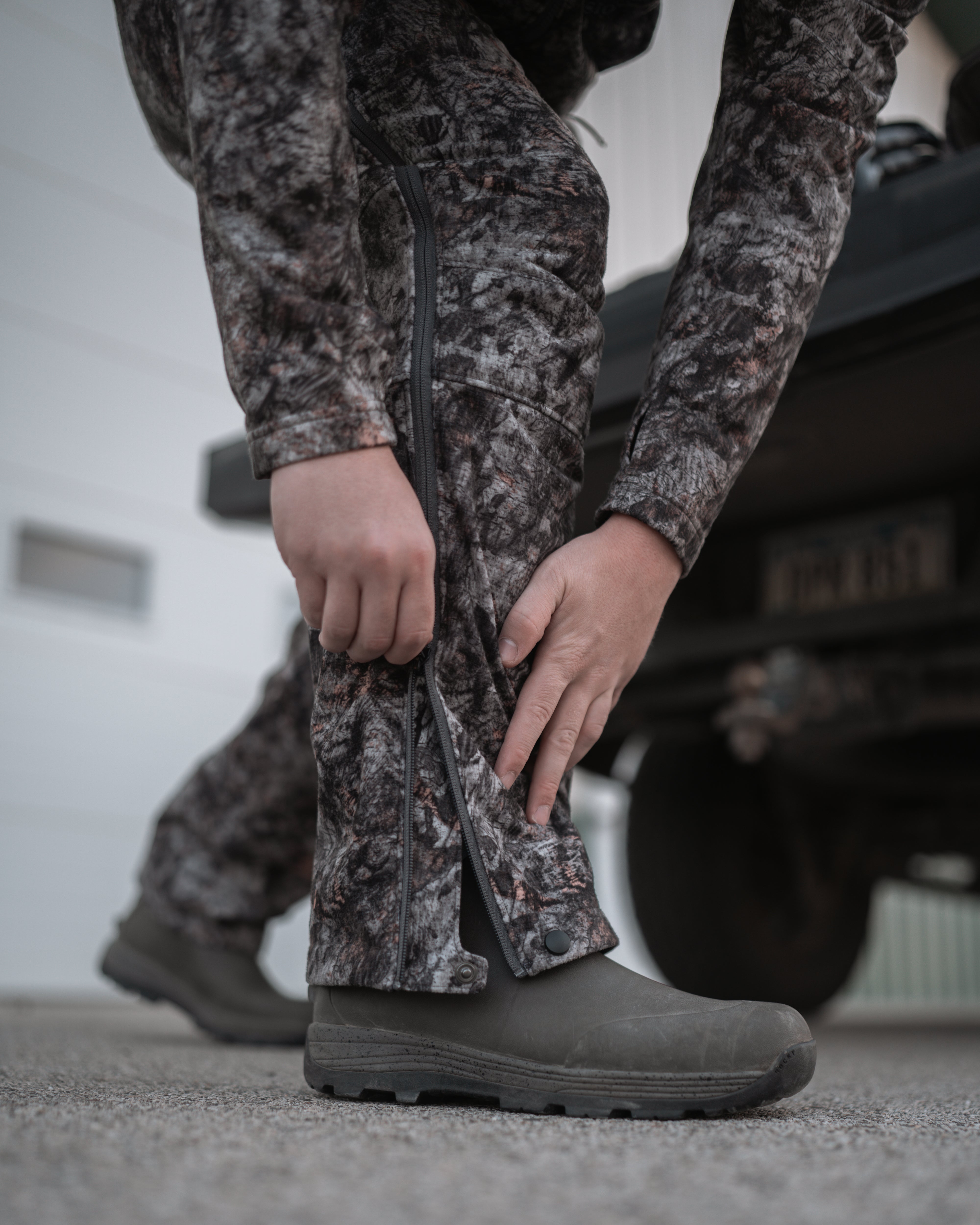 hunter using full side zipper on midweight sherpa bowhunting bib in raptor camo
