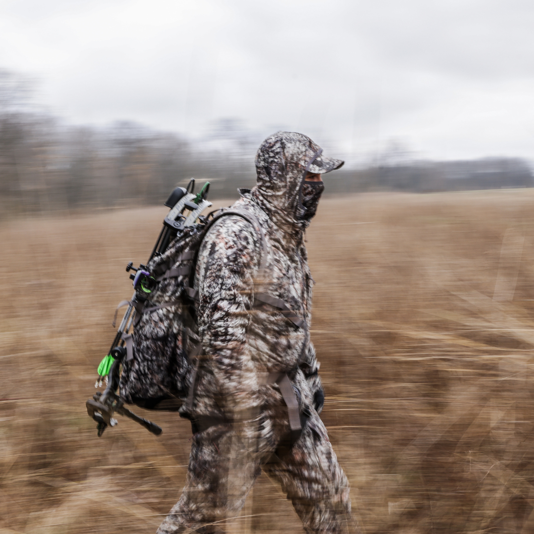 Person in full ASIO Gear raptor camouflage gear walking through a field with a blurred background showing off windproof hunting jacket