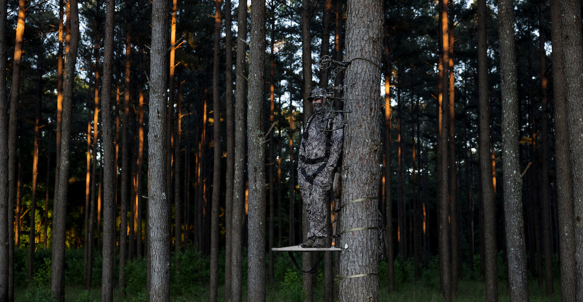 asio gear hunter wearing raptor camo blending into a group of pines trees in early season