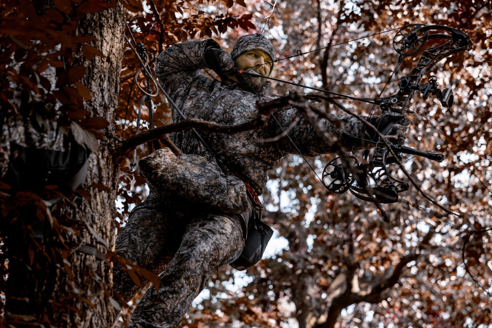 bowhunter wearing asio gear windproof hunting jacket with bow hunting collar in asio raptor camo while hunting whitetail deer